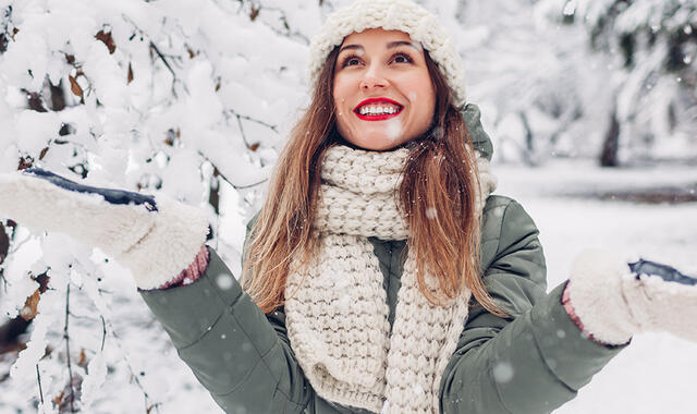 Kvinna står i vinterlandskap, glad, har släppt stress. 