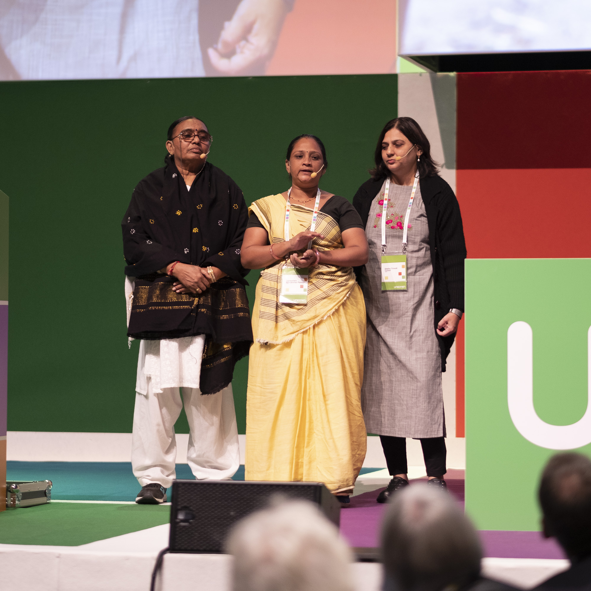 Bild på Shalini, Jignasa och Ramila när de står på scen på Unionens kongress.