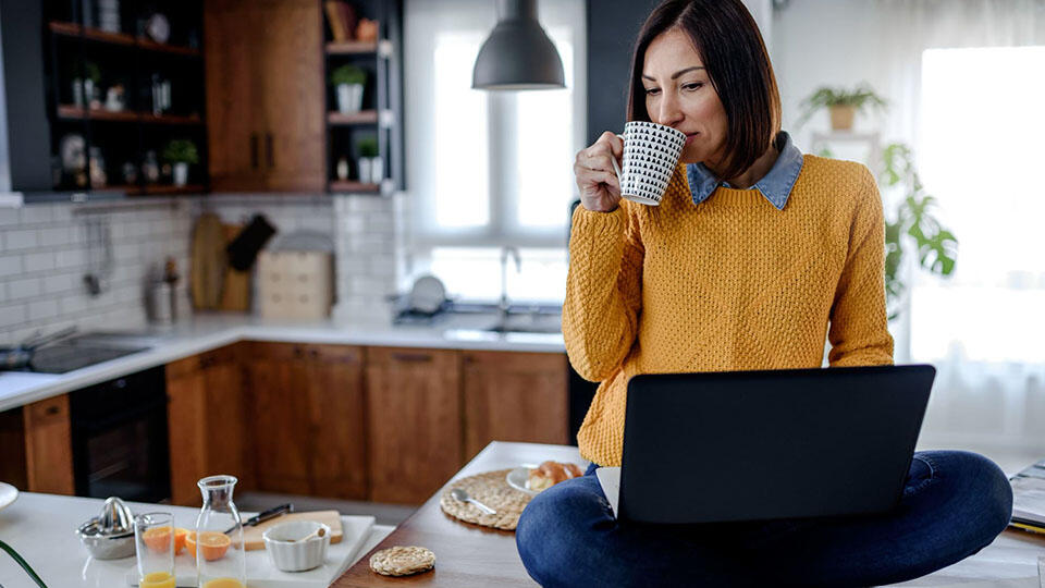 Person med laptop i knät sittandes på en köksbänk