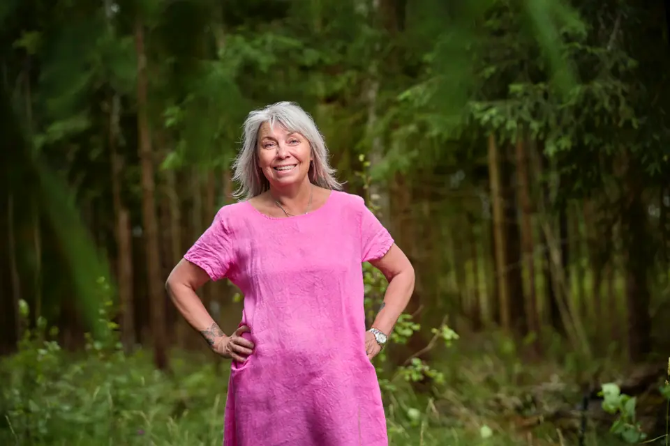 Medelålders kvinna, glad, i rosa klänning, skog i bakgrunden 