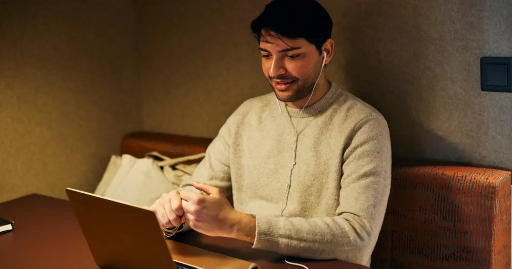 Ung man sitter med sin laptop vid ett bord.