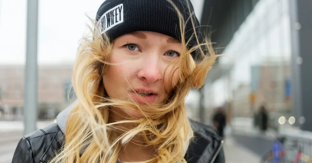 Ung kvinna med mössa på sig tittar in i kameran från nära håll.