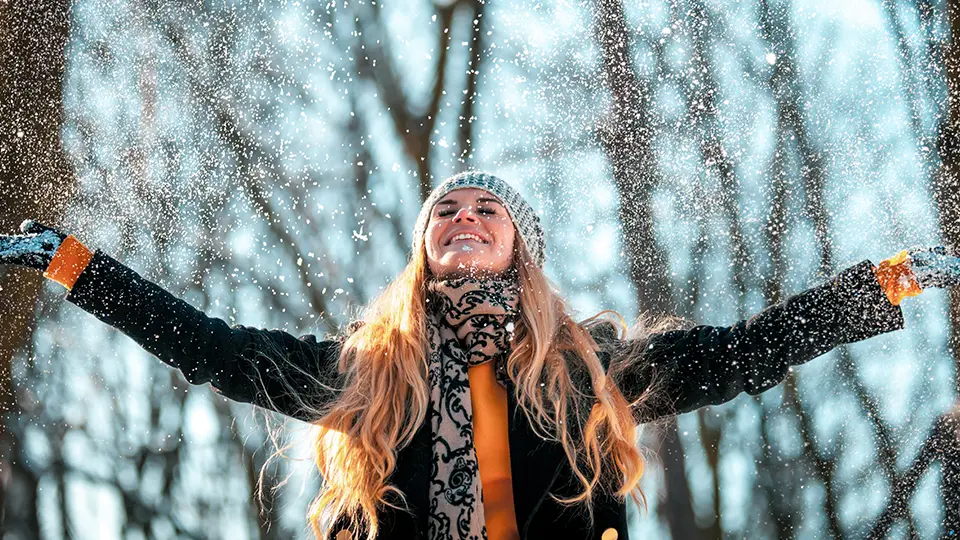 Kvinna som står i vinterlandskap och är glad. 