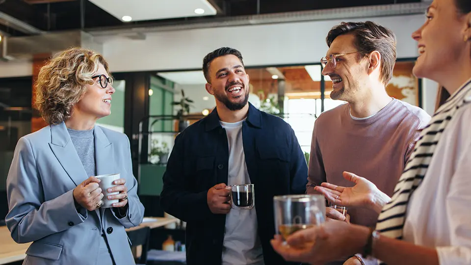 Fyra kollegor står vid kaffeautomaten och ser ut att ha ett trevligt samtal. 