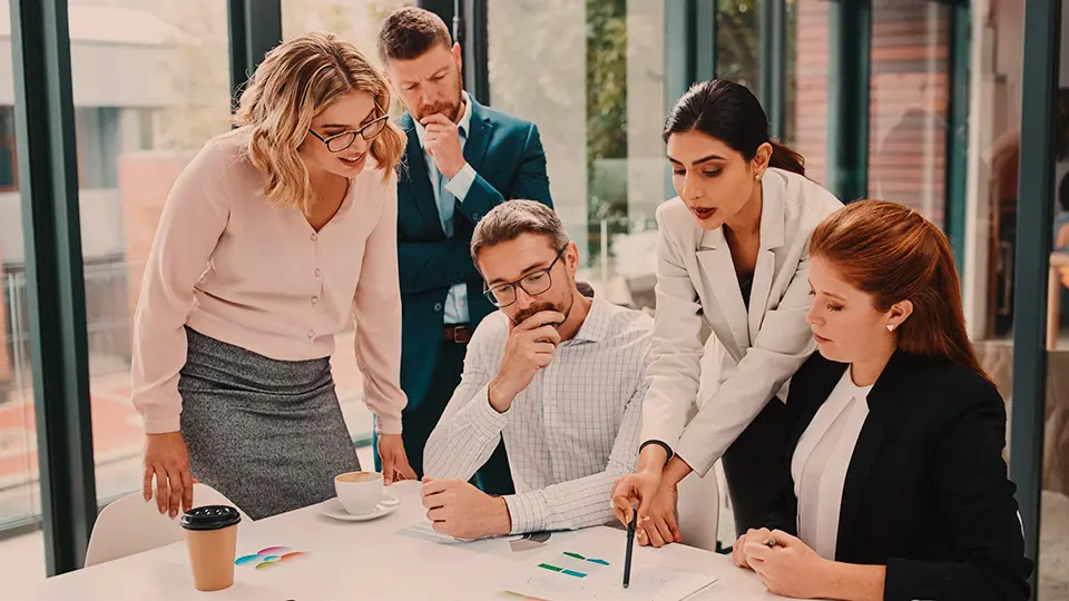 En grupp människor står runt ett skrivbord och tittar på ett dokument