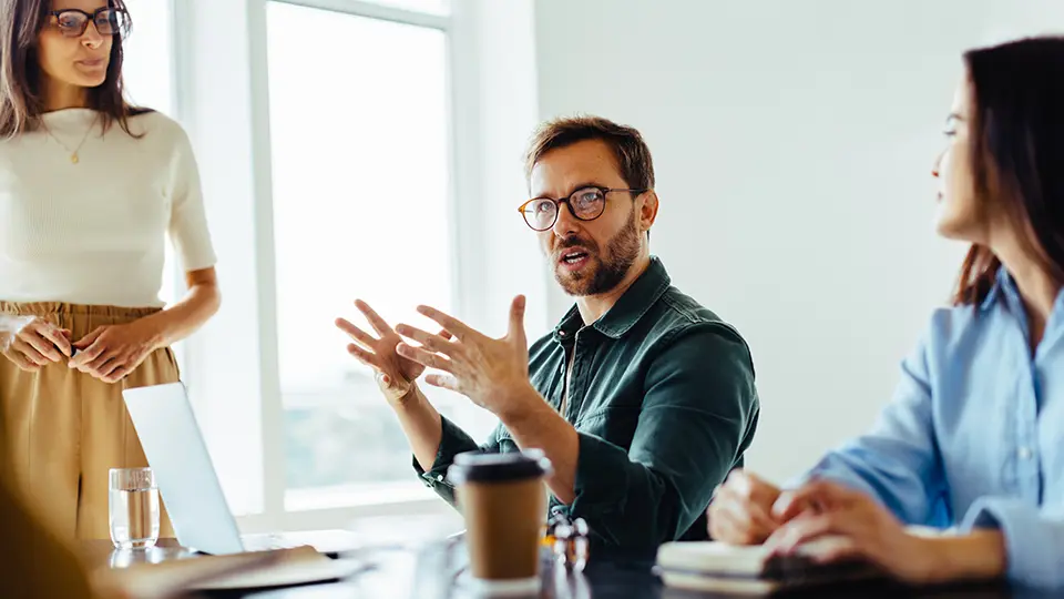 Man och två kvinnor sitter vid konferensbord och pratar. 