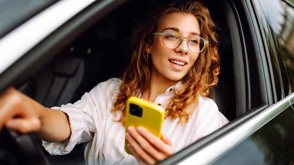 Kvinna i modern bil, med mobiltelefon i handen.