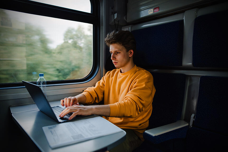 Man som sitter på ett tåg med sin dator