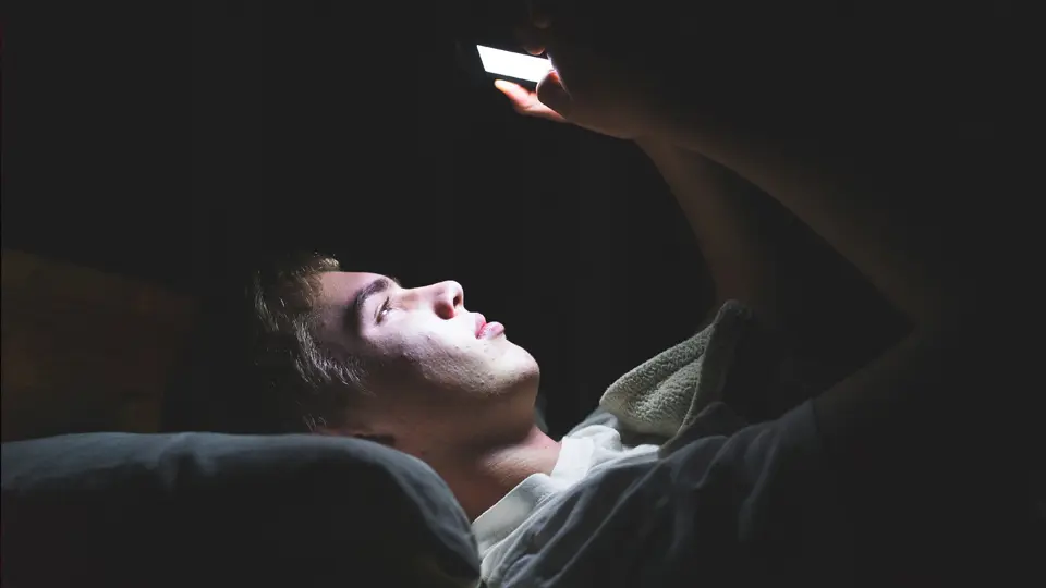 Person som ligger och tittar på mobilen i mörkret