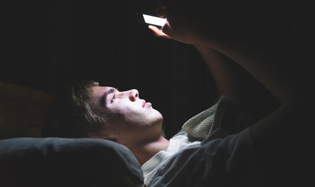 Person som ligger och tittar på mobilen i mörkret