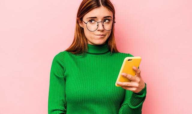 Kvinna mot rosa bakgrund, med gul mobil i handen
