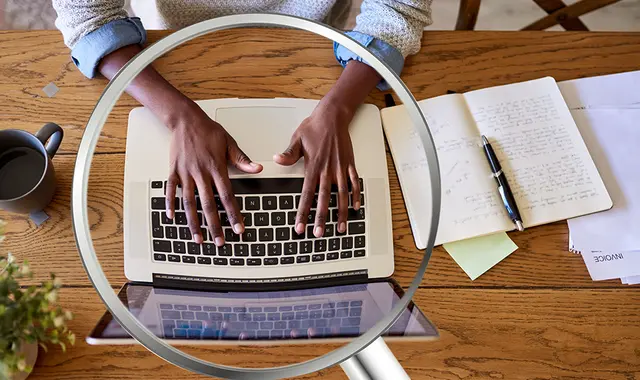 Någon tittar i förstoringsglas på vad kvinna skriver på datorn.