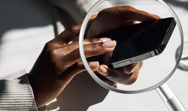 Någon iakttar, via förstoringsglas, vad person skriver på mobilen. 