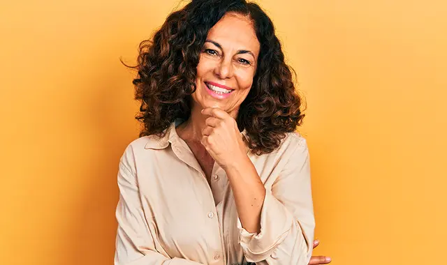 Glad medelålders kvinna mot gul vägg. 