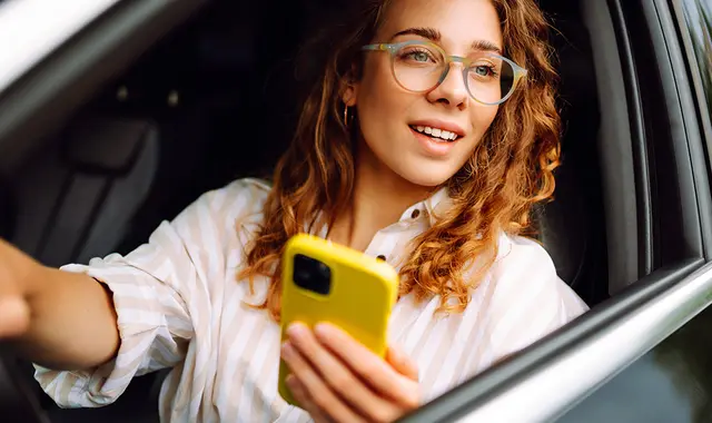 Kvinna i modern bil, med mobiltelefon i handen.