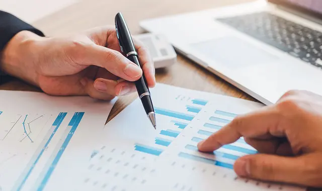 Bild på ekonomiska staplar, händer och penna. 