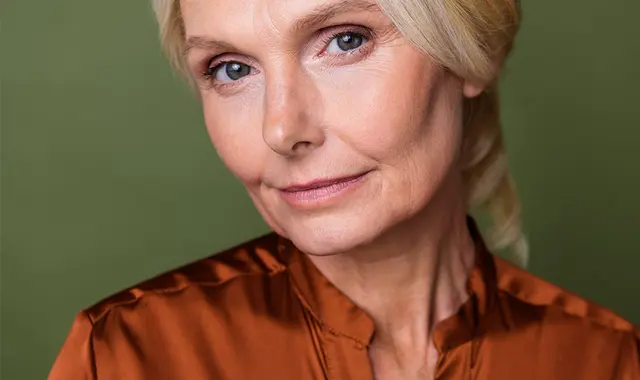 Medelålders kvinna mot grön vägg. 