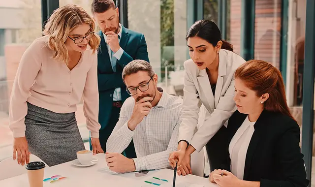 En grupp människor står runt ett skrivbord och tittar på ett dokument