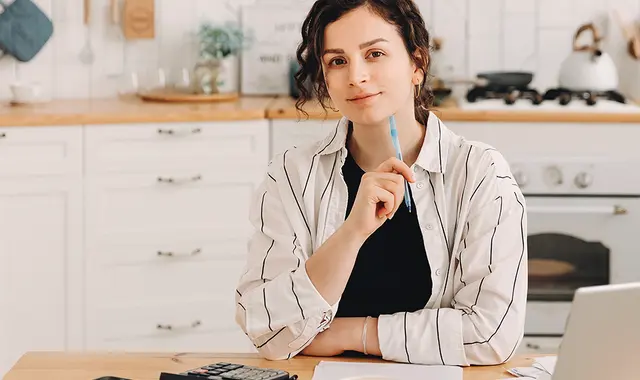 Kvinna i vit skjorta sitter i vitt kök och planerar budget