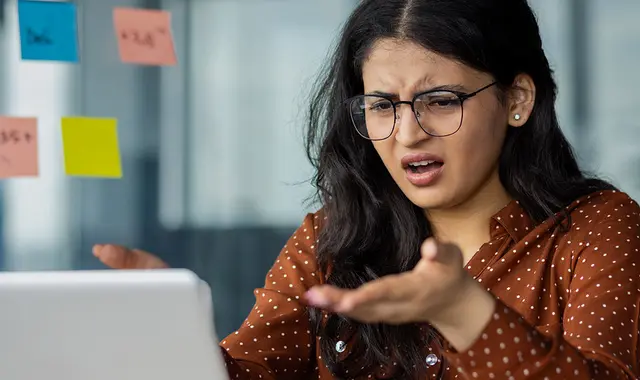 Kvinna i brun skjorta är arg på en dator som trasslar. 