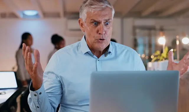 Man i blå skjorta sitter framför dator och studerar. 