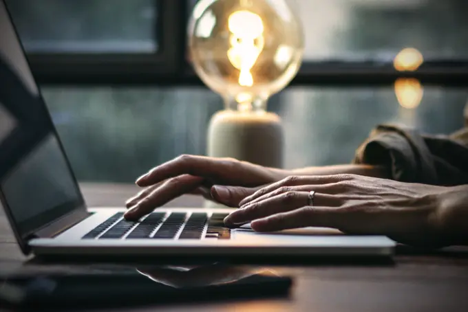 Händer som skriver på en dator och en lysande lampa bakom