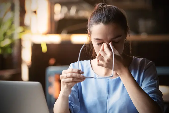 Person som har tagit av sig glasögonen och tar sig i ansiktet