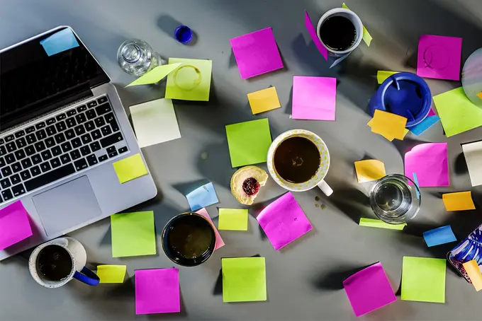 Dator med många post it-lappar och kaffekoppar bredvid