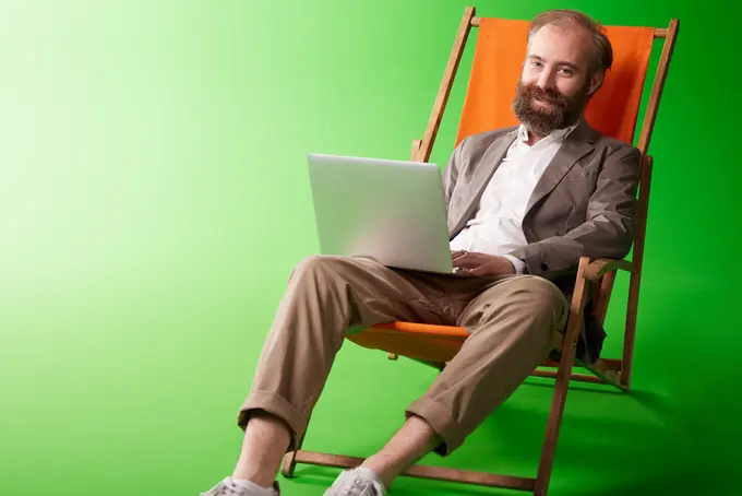 Men som sitter i solstol och har en laptop i knät.