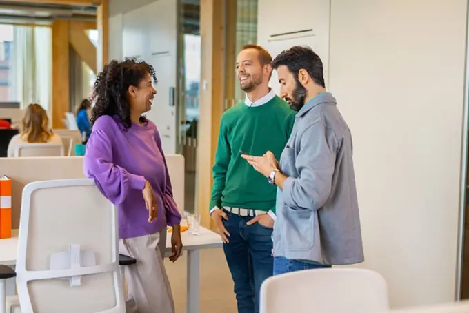 Tre kollegor pratar och skrattar i kontorsmiljö