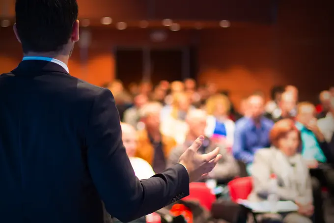 Foto på person som talar inför publik i mötessal