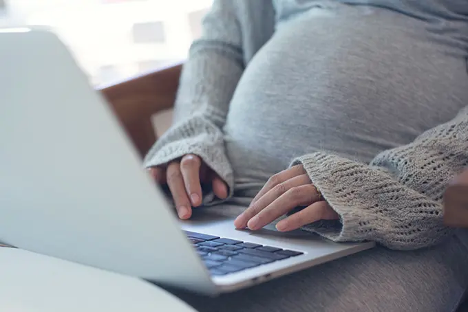 Gravid kvinna jobbar på laptop.