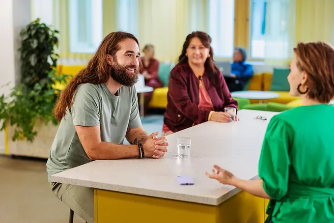 3 glada personer i samtal runt ett bord