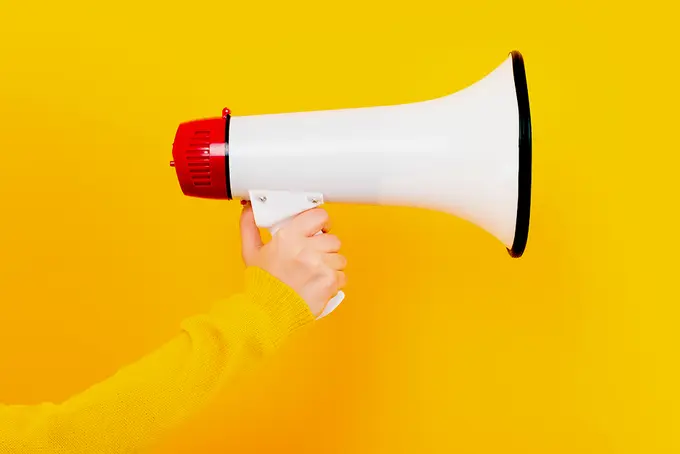 Megafon som hålls upp mot gul bakgrund.