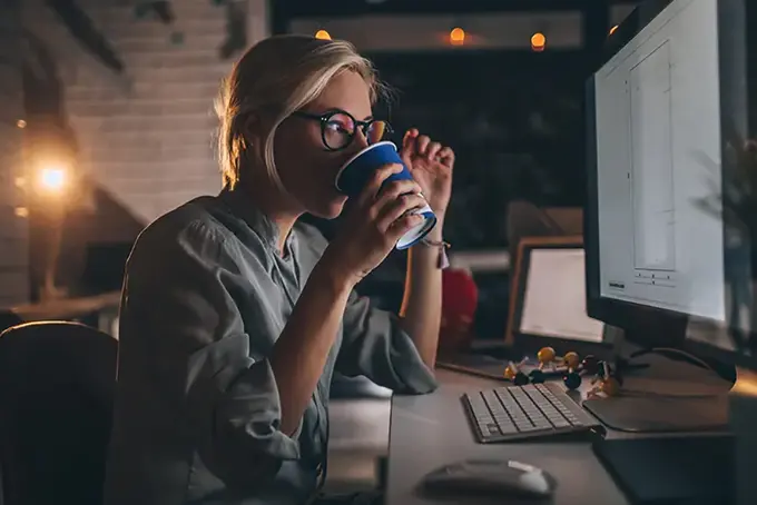 Ung kvinna nyanställd på nya jobbet, med kaffe framför datorn. 