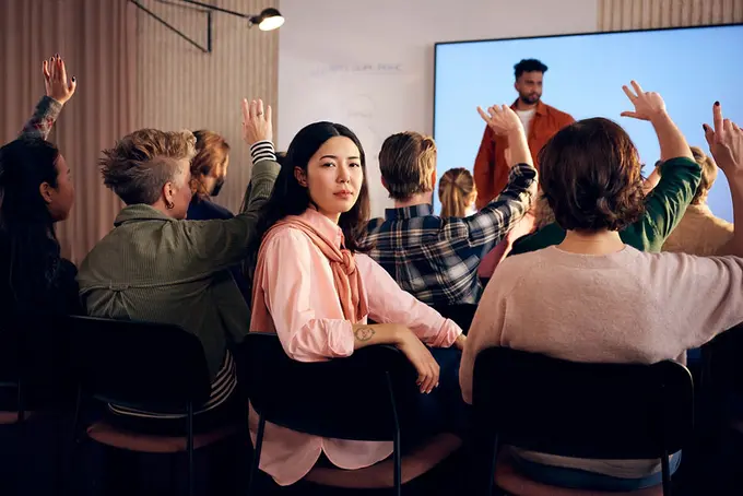 Ung person tittar in i kameran under gruppmöte i föreläsningssal