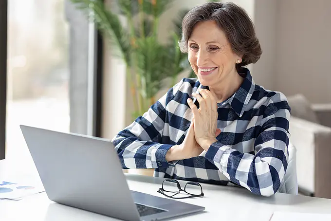 Leende person sitter vid sin laptop och ser nöjd ut