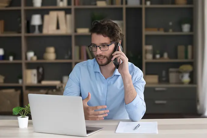 Man som pratar i telefon och samtidigt tittar på datorskärm
