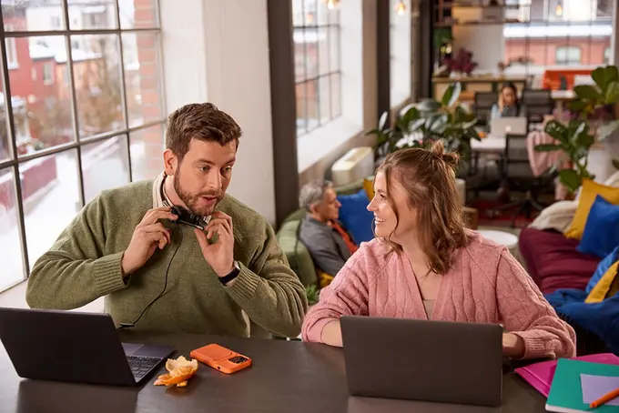 Två kollegor som pratar med varandra med datorer framför sig