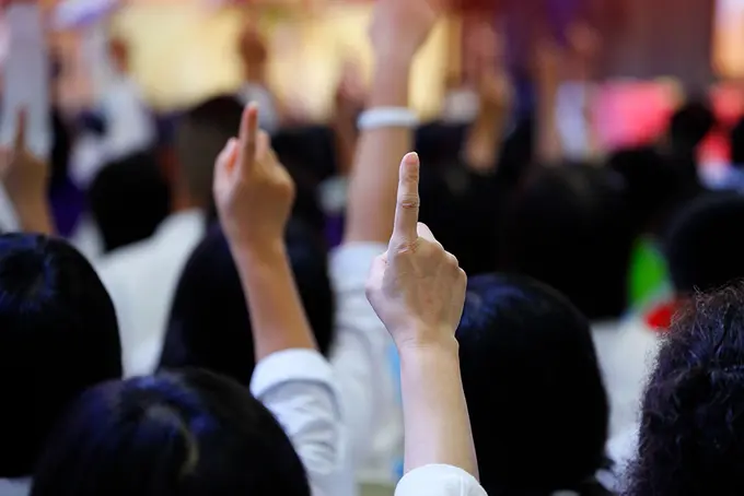 Händer sträcks upp för att säga något i en fullsatt sal