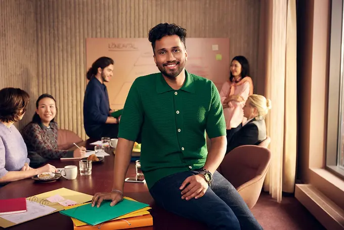 Man som sitter på skrivbord, med kollegor i bakgrunden