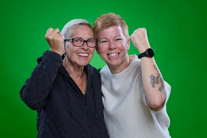 Två kvinnor mot grön bakgrund med knutna nävar och leenden