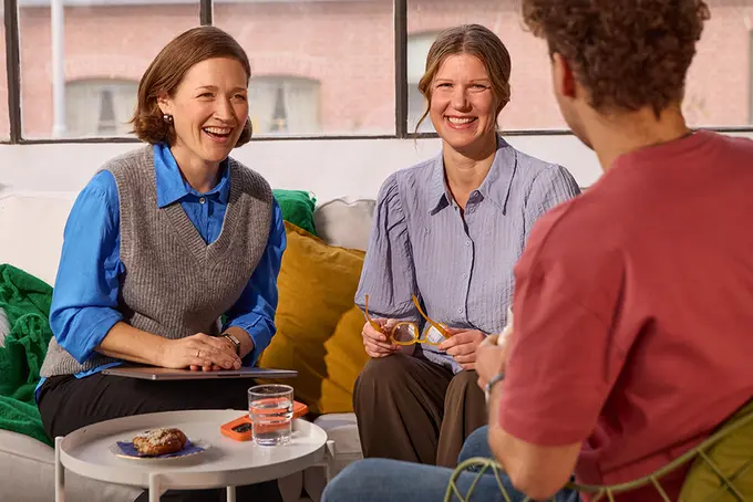 Tre personer sitter i glatt samtal vid ett fikabord. 