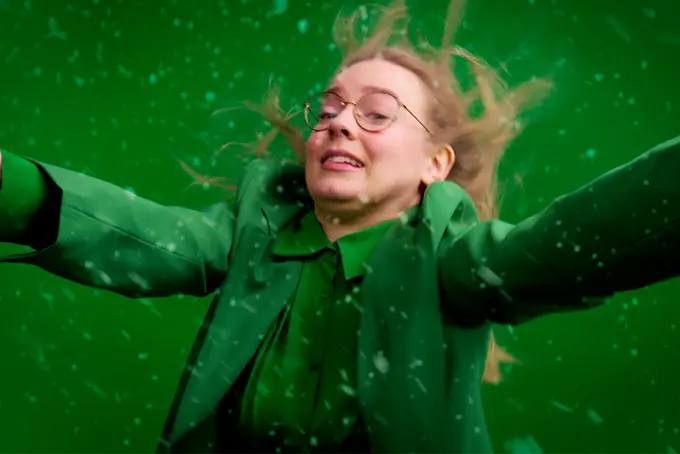 Kvinna klädd i grönt framför grön bakgrund som ser ut att nästan blåsa bort.