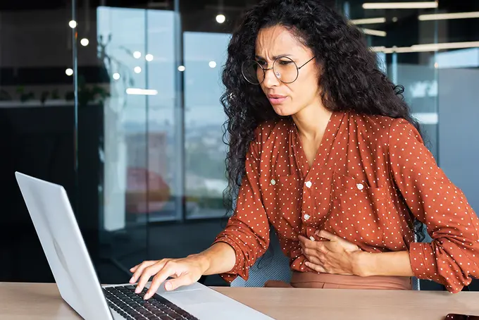 Kvinna som har mensvärk när hon sitter vid sin arbetsplats.