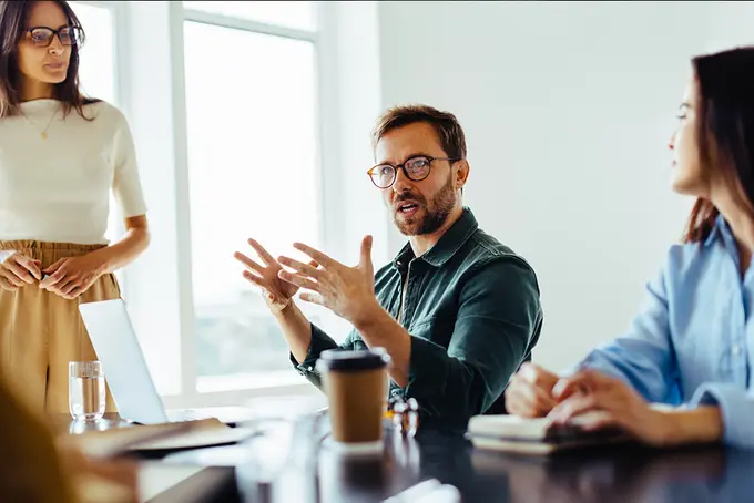 Man och två kvinnor sitter vid konferensbord och pratar. 