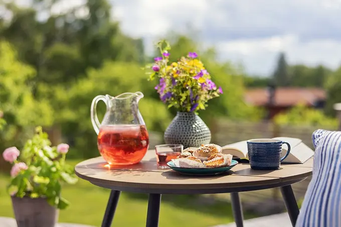 Somrigt frukostbord utomhus med saft, kaffe, bakverk och bok – symbol för semester och avkoppling.