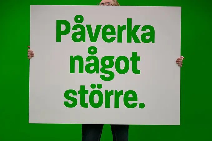 Person med gigantisk skylt med texten "Påverka något större". 