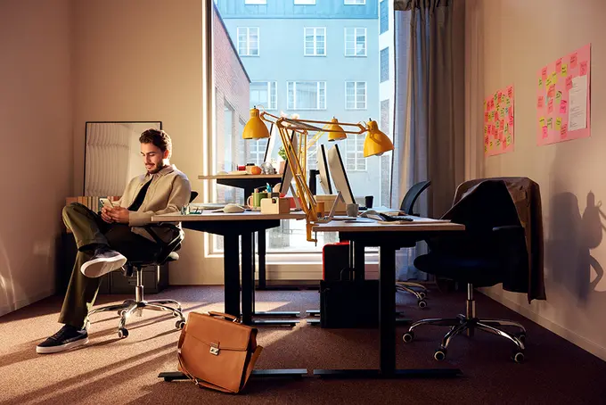 Ung man som sitter på kontorsstol och tittar på mobilen